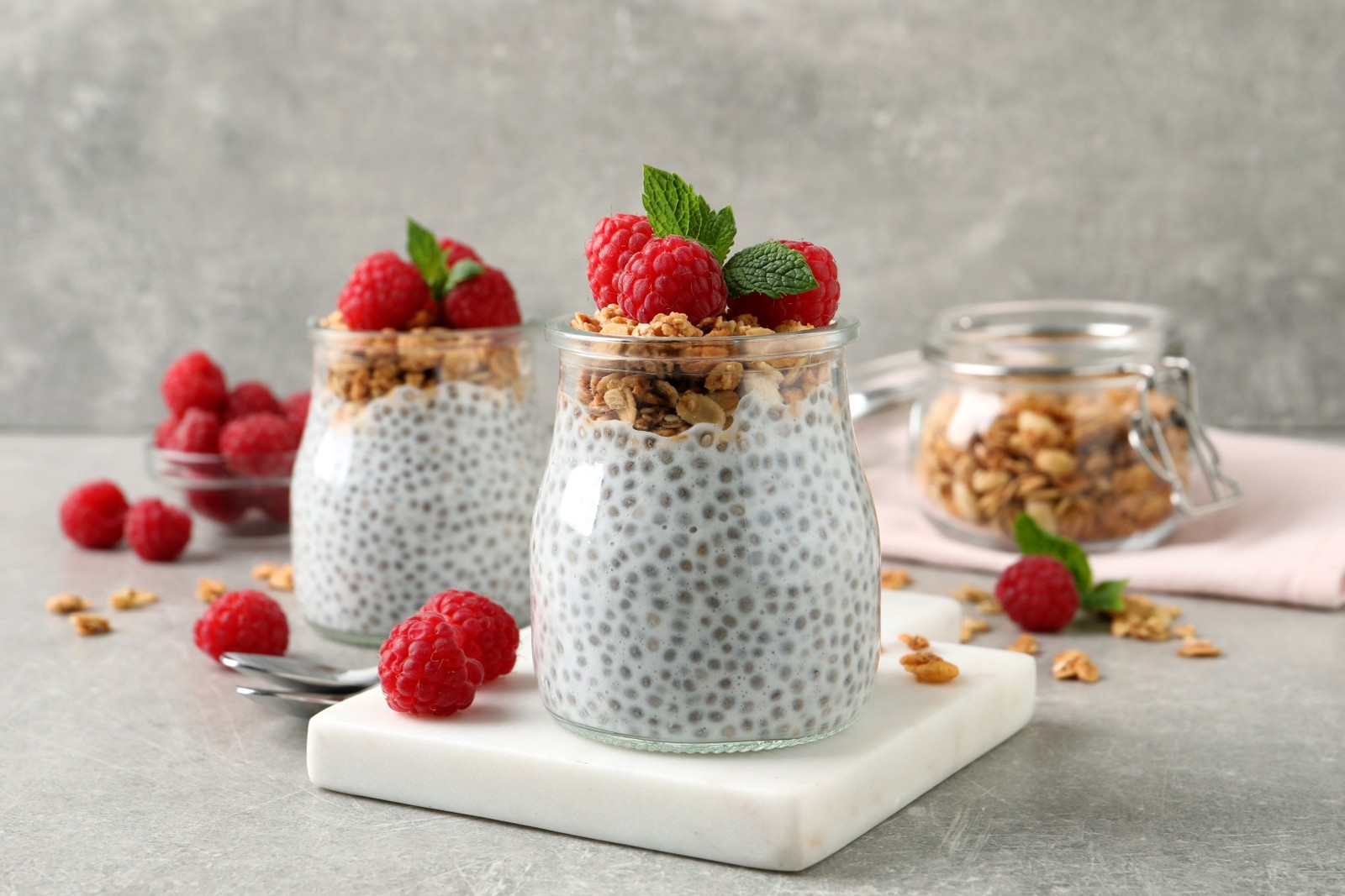 Photo of delicious chia pudding with raspberries and granola on grey table
