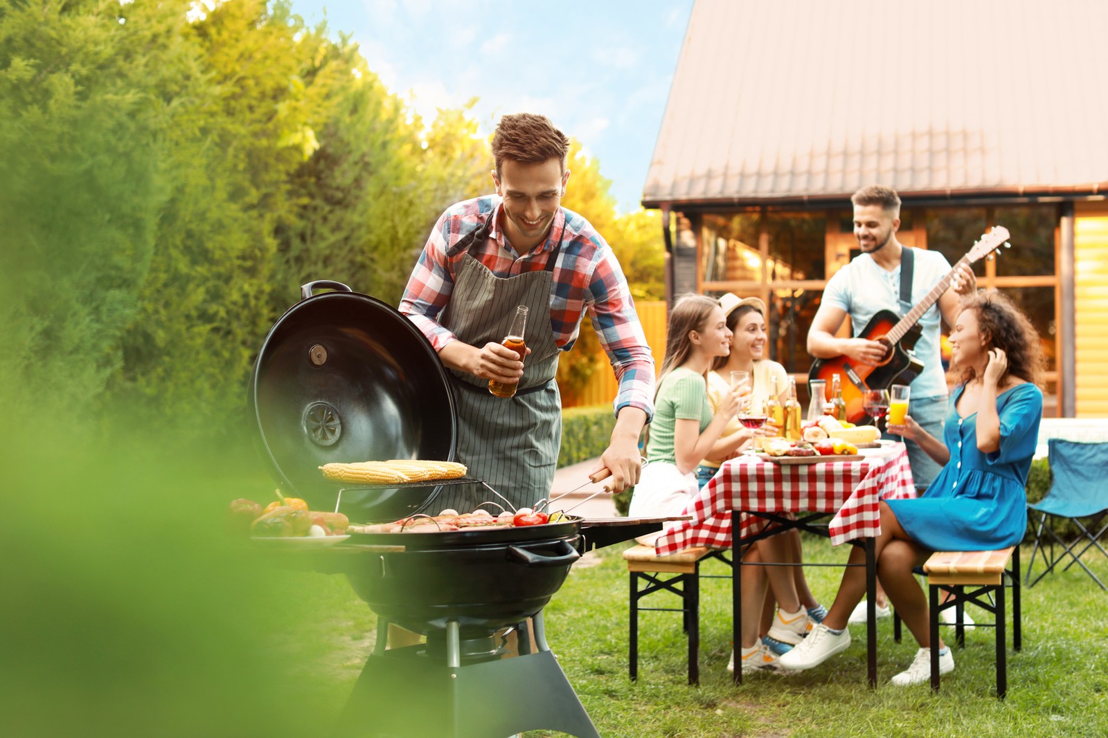 Photo of group of friends at barbecue party outdoors. Young man near grill