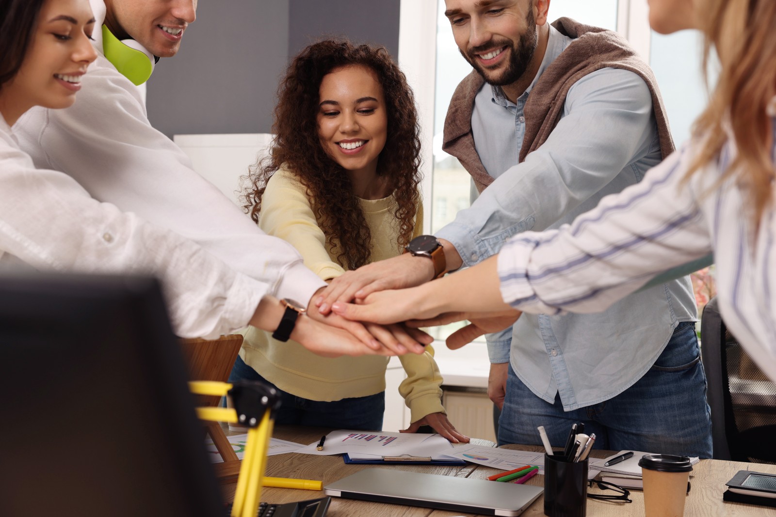 Photo of team of employees putting hands together in office. Startup project