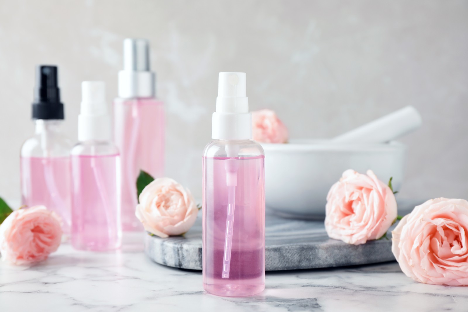 Photo of bottles with rose essential oil and flowers on marble table