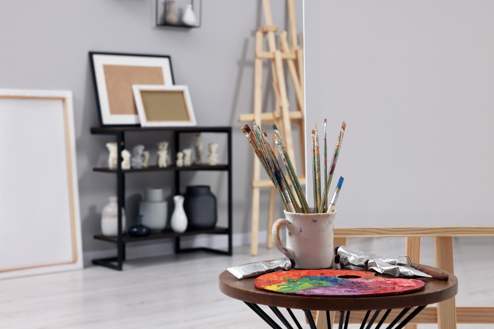 Photo of wooden easel with canvas near paints, palette and brushes in artist's studio, space for text