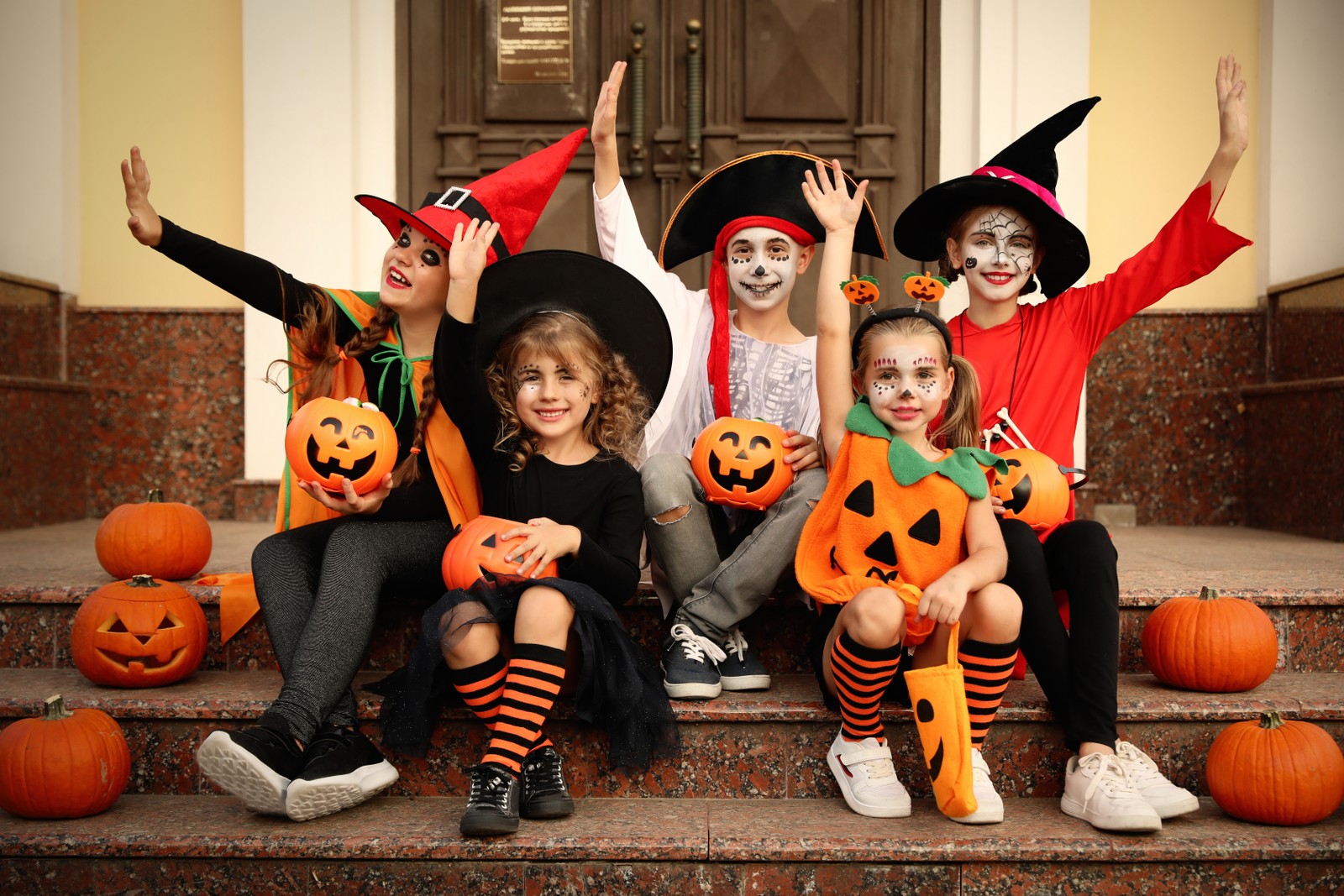 Photo of cute little kids with pumpkins wearing Halloween costumes on stairs outdoors
