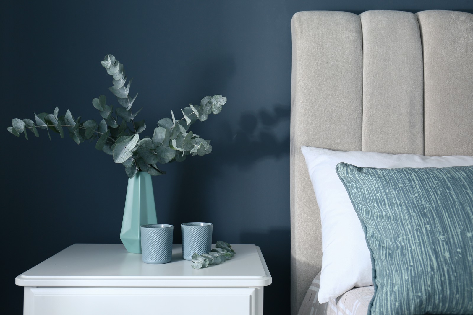 Photo of beautiful eucalyptus branches and candles on nightstand in bedroom. Interior element