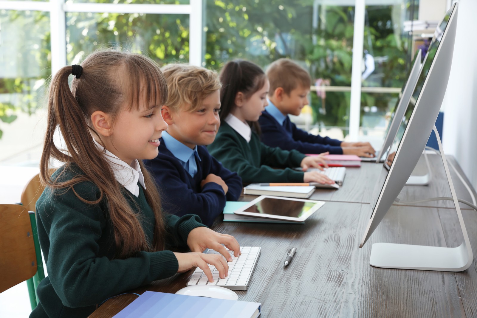 Photo of little children in stylish school uniform at desks with computers